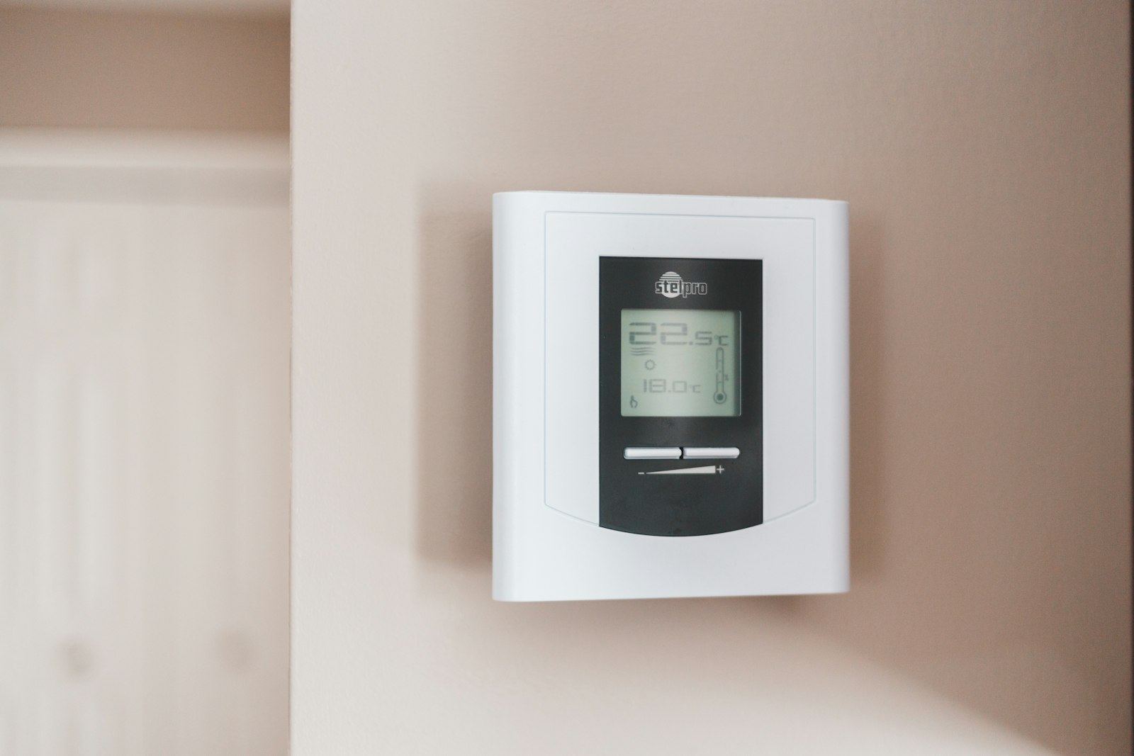 A white digital room thermostat on a wall